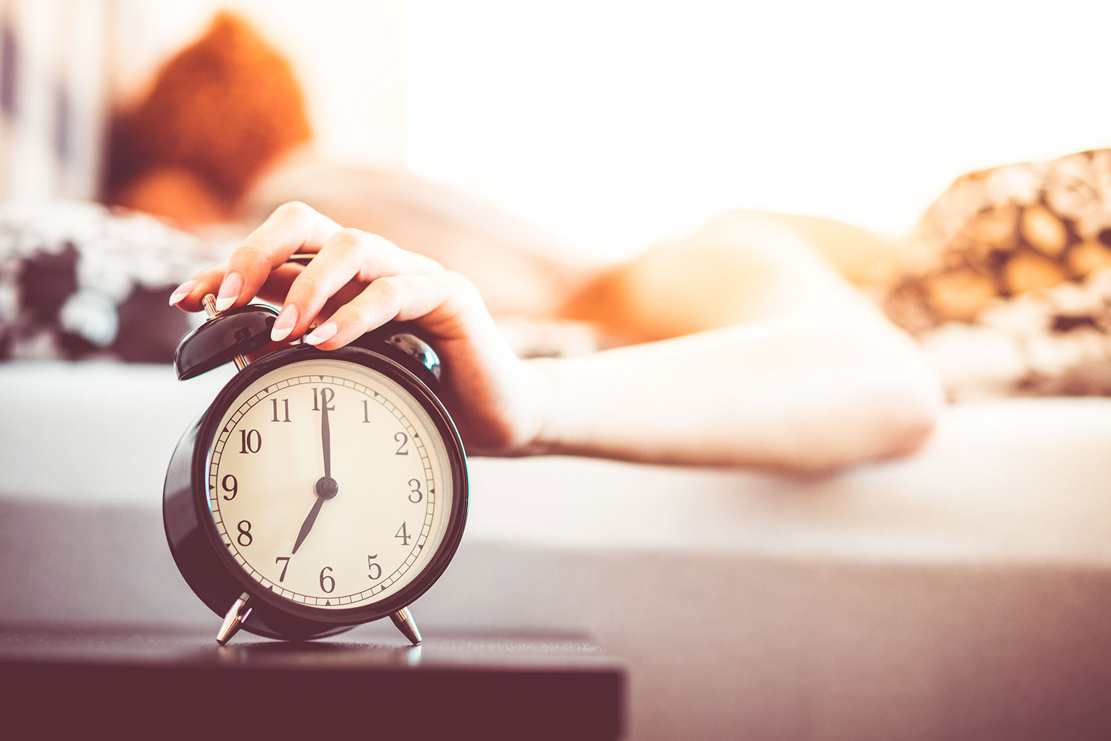 Woman Shutting Off Ringing Alarm Clock From Bed